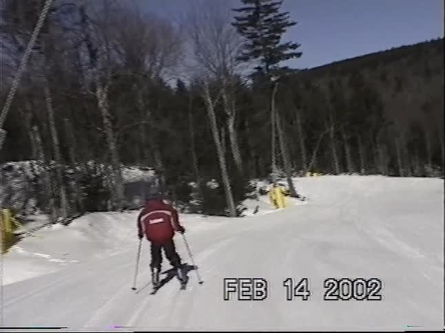 Vintage home movie footage captures a skier gliding down a sunny, groomed mountain slope in 2002
