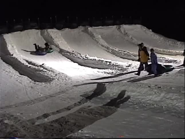 A group of people enjoy a fun night of snow tubing down an illuminated, snowy hill at a winter resort