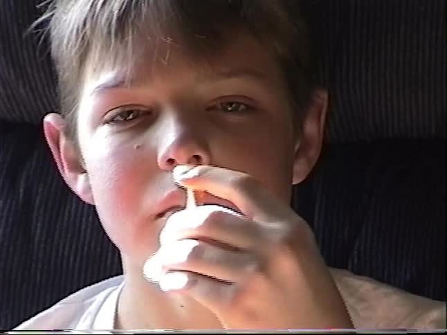 Vintage home video footage shows a close-up of a young boy eating potato chips from a can while relaxing in a chair