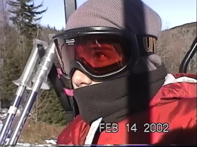 Close-up vintage camcorder footage of a skier in a red jacket riding a chairlift on a sunny winter day