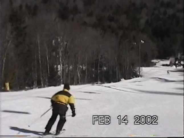 A first-person view follows a skier in a yellow jacket down a sunny mountain slope in this vintage 2002 footage