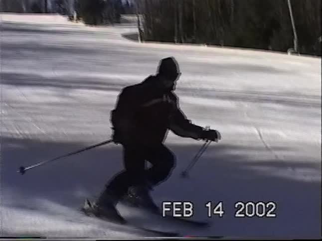 Vintage home video footage from 2002 shows a person skiing down a snowy mountain slope on a sunny day