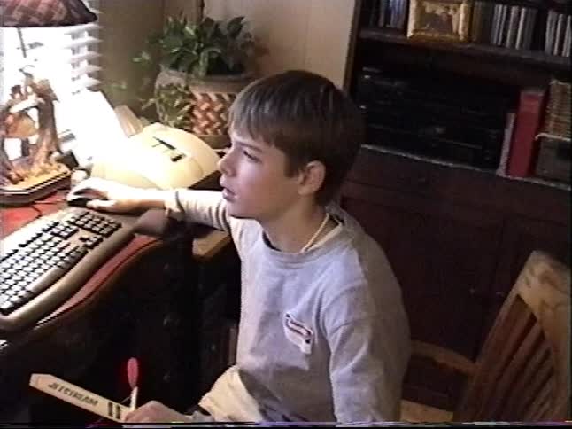 A young boy smiles at the camera before turning back to his vintage desktop computer in this nostalgic home video from the 1990s