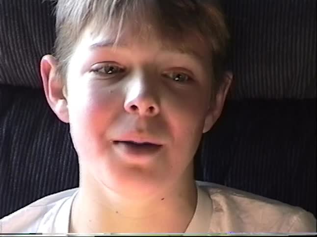Vintage VHS footage captures a young boy relaxing in a recliner chair and eating potato chips from the can