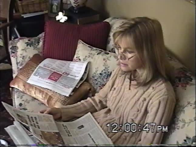 A woman reads the Thanksgiving newspaper on a floral couch while her dog sits patiently beside her in a cozy living room in this 2002 home video