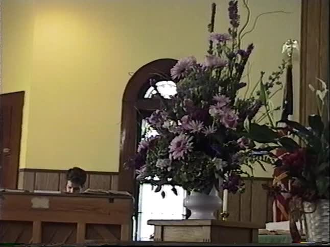 A view from the pews of a pianist singing during a church service, with a large floral arrangement in the foreground