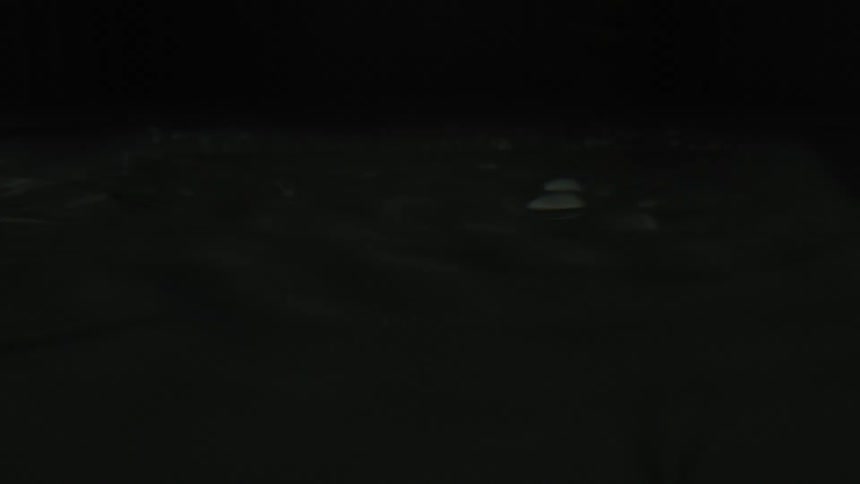 A close-up, slow-motion shot of a water drop creating ripples on a dark, still surface