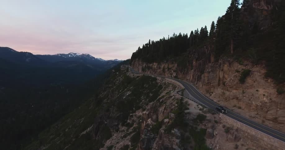 Car driving down a mountain highway at sunset