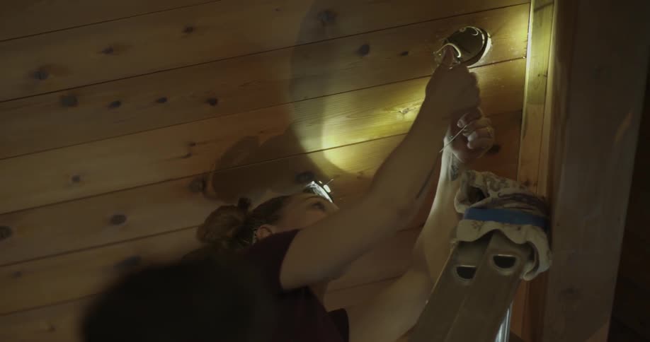 Woman taping some wires coming from a hole in a ceiling