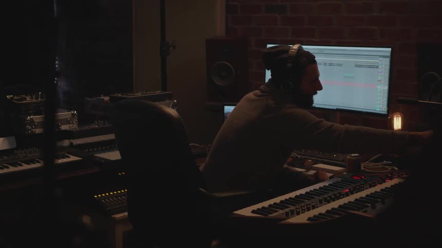 A man is working in a music studio adjusting knobs and using a computer