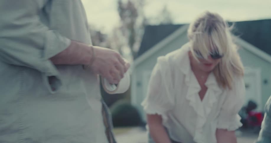 Close-up slow-motion shot of a man's hands struggling to find the end of a roll of packing tape in a suburban driveway
