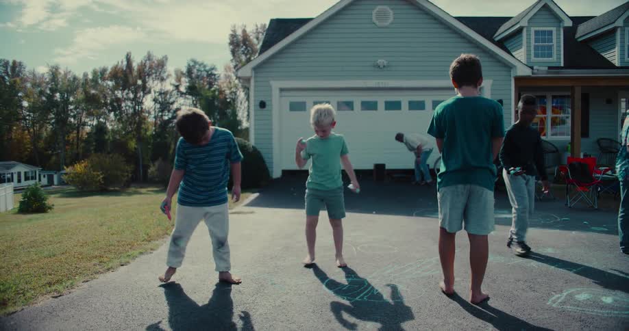 A group of young boys play together and draw with sidewalk chalk on a suburban driveway on a sunny day