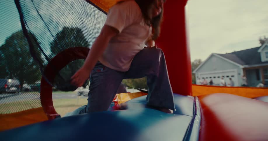 A happy young girl smiles as she climbs into a colorful bounce house during a party in slow motion