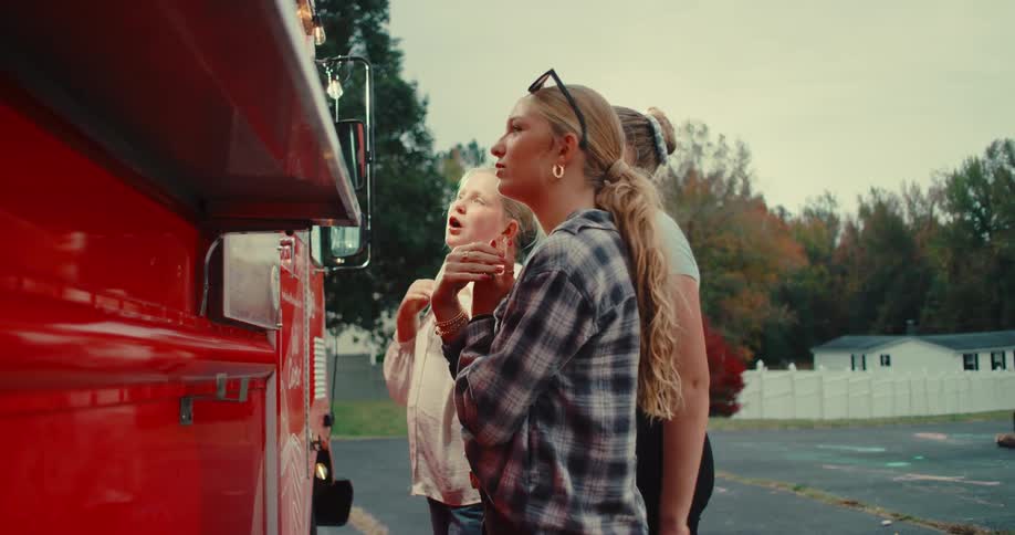 Three women of different ages stand together, excitedly discussing the menu and ordering from a vibrant red food truck