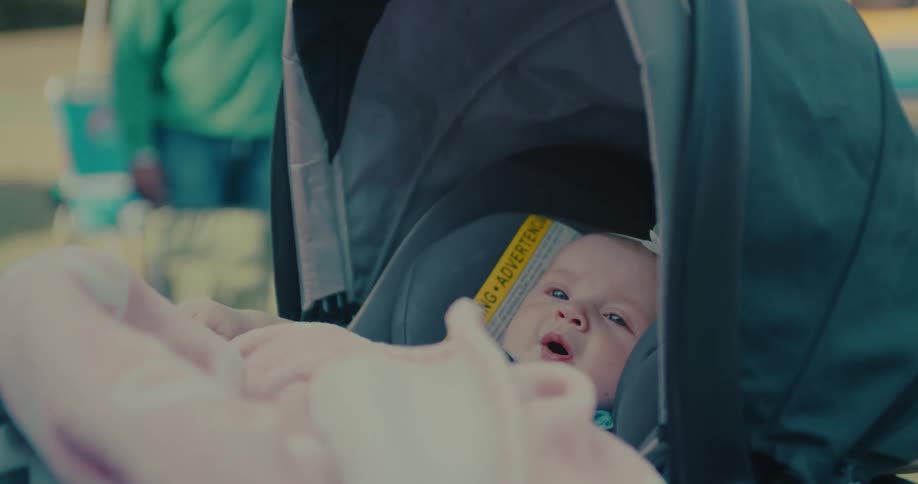 A cute newborn baby girl in a car seat carrier begins to get fussy and cry while outdoors