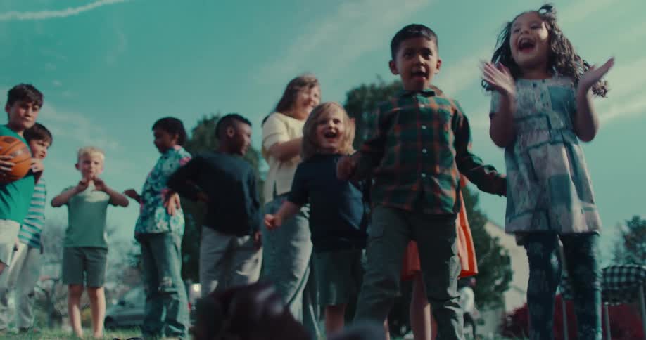 A diverse group of excited children stand together outdoors, their faces filled with joy and wonder as they look up at the sky