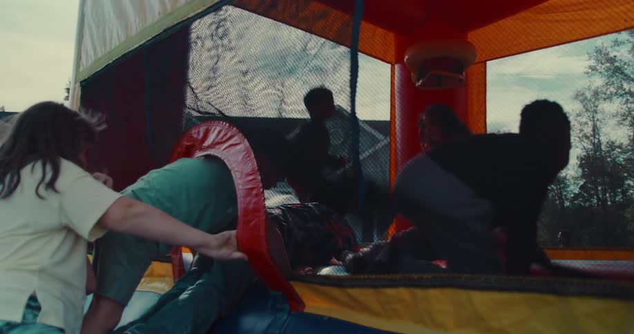 A diverse group of kids energetically jump and play together inside a colorful bounce house in slow motion