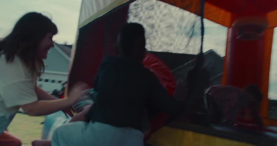 A group of diverse and energetic children jump, laugh, and play together inside a colorful bouncy castle in slow motion