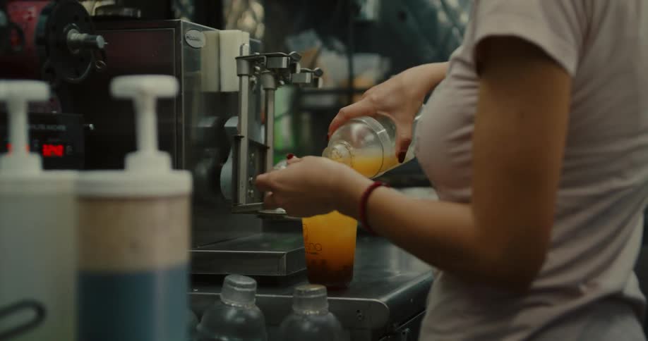 A barista carefully pours a freshly shaken iced tea into a cup of boba pearls in slow motion