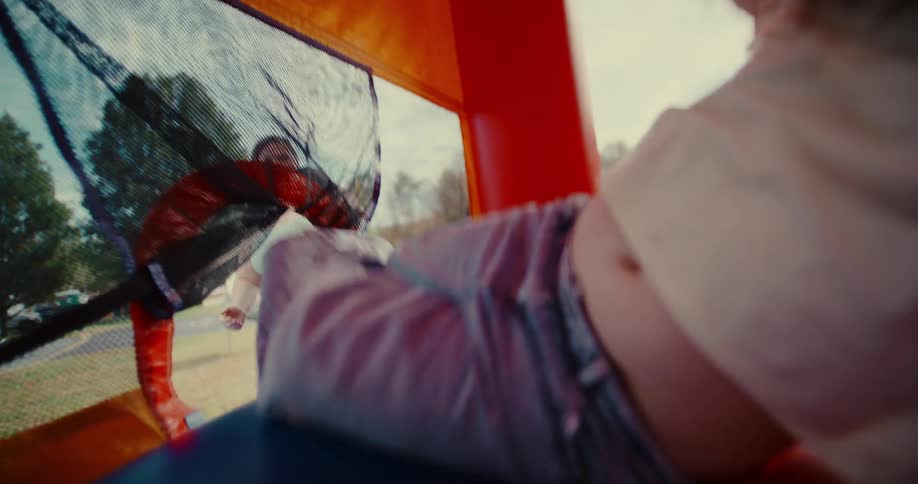 A mother watches as her young daughter joyfully jumps in a colorful bouncy castle in slow motion