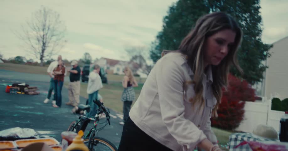 A woman carries a tray of freshly grilled food to a table and prepares buns for a lively neighborhood block party in slow motion