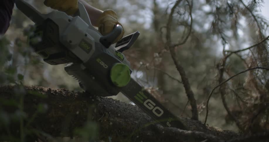 A woman is using a chainsaw to cut branches from a fallen tree
