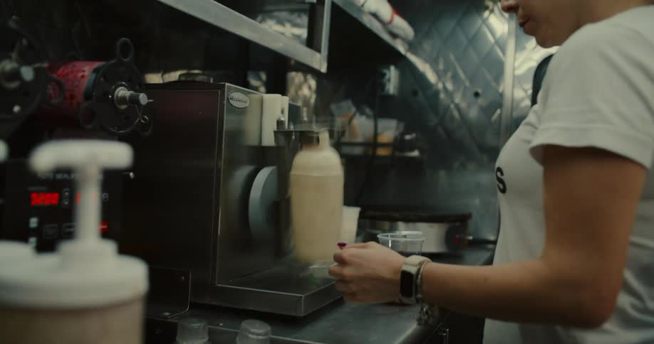 A female barista uses an automatic drink shaker to mix a beverage while preparing boba tea in a food truck kitchen
