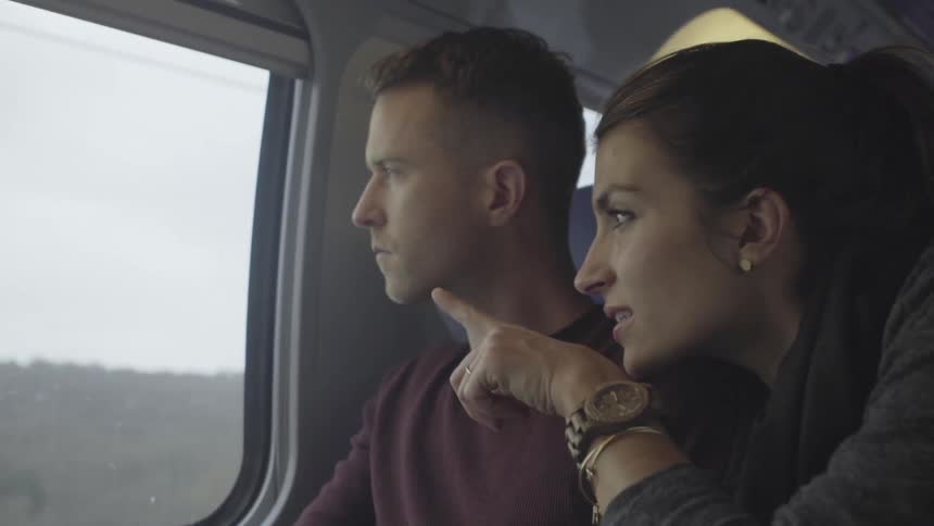A woman and man look out of a train window while traveling