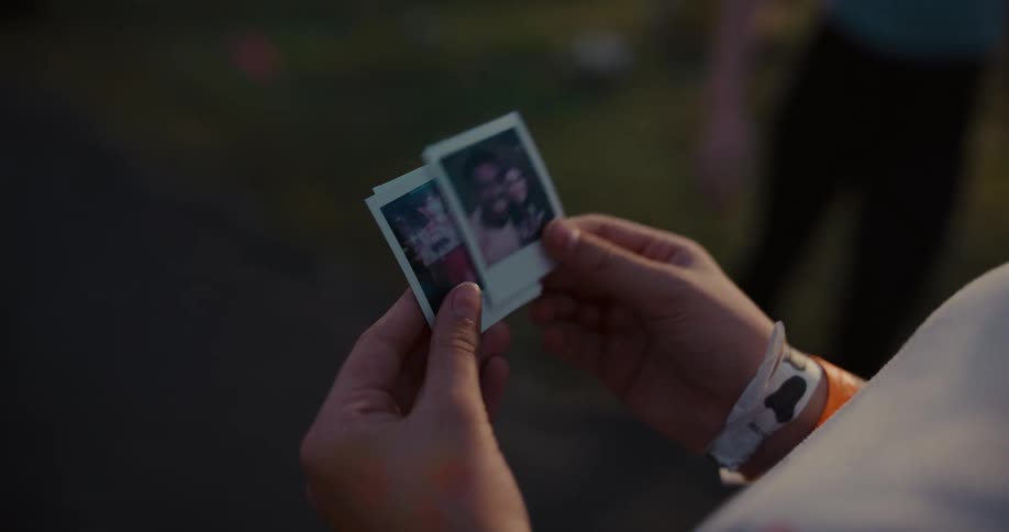 Close up on hands fondly looking through a stack of instant photos, cherishing memories from a festival at dusk