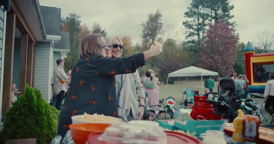 Three women smile and take a selfie together at a lively outdoor family party