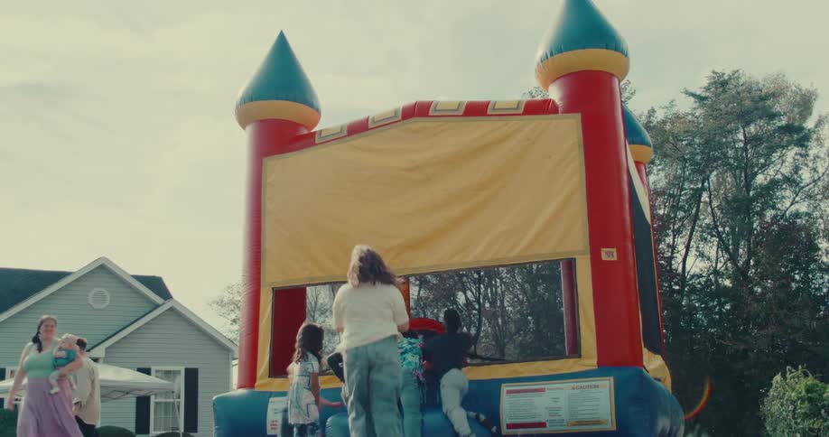 A colorful bounce house inflates in a backyard as excited children and their families watch in anticipation