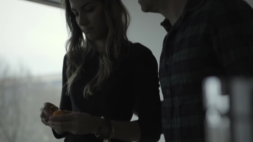 A couple talk in a kitchen while peeling oranges