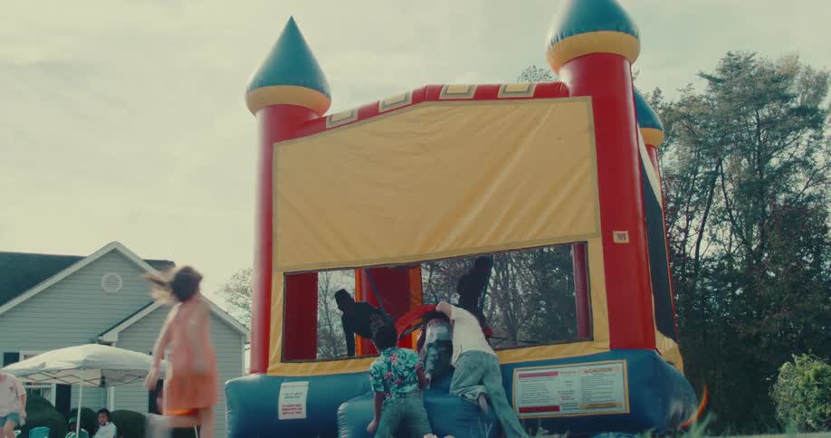 Happy children jump and play together in a colorful inflatable bounce house at an outdoor party in slow motion