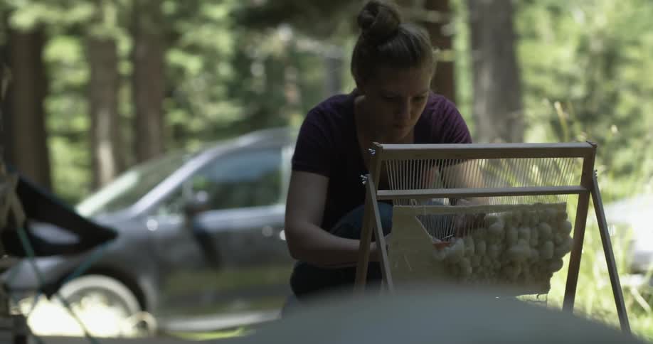 A woman is working at a loom set up outside