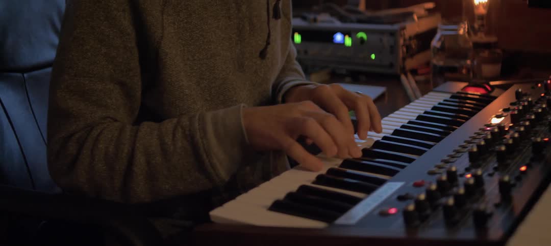 A person is playing a keyboard in a studio full of equipment