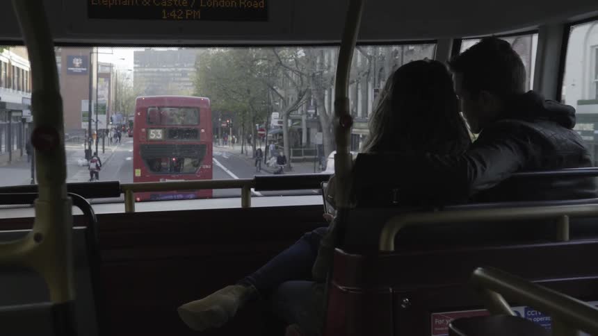 A man and a woman sit close together as they ride a bus in london