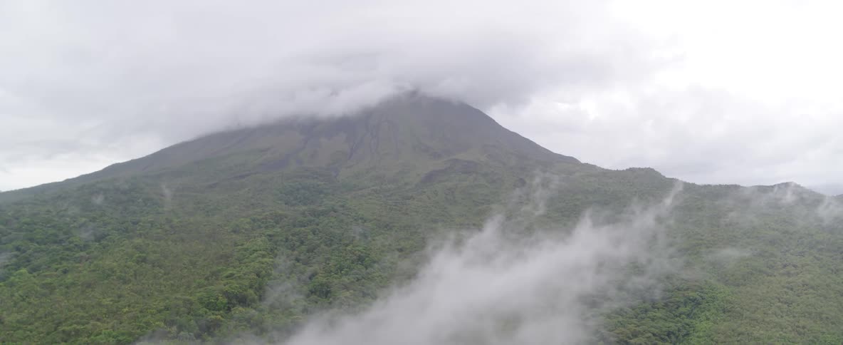 A static shot shows a lush green volcano with its peak shrouded in thick clouds and fog