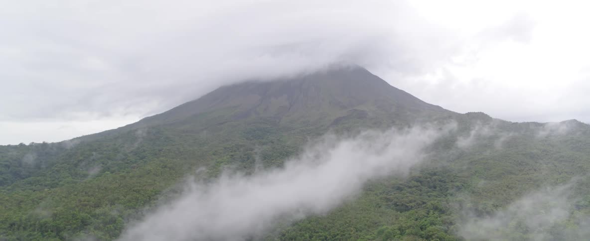 A serene, static shot captures a majestic volcano, its peak hidden by a thick blanket of clouds and mist