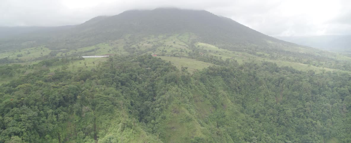 A misty aerial view of a vast, lush green mountain range covered in dense tropical forest under a cloudy sky