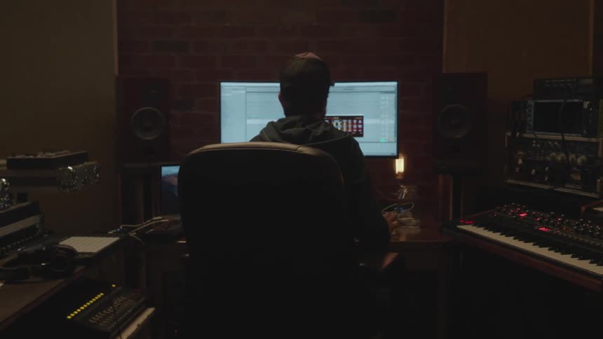 A man sits in front of a computer in a studio making music