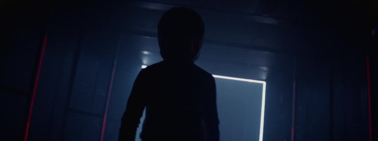 A motocross rider in full gear and helmet is revealed by flashing lights in a dark, futuristic laser tunnel