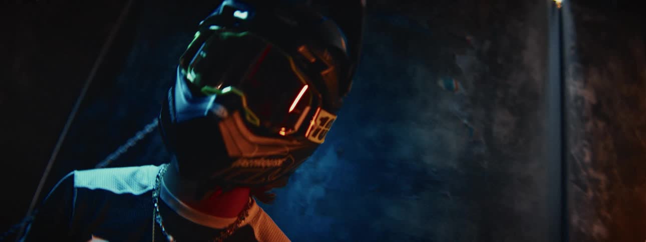 Close-up of a motocross rider wearing a helmet and goggles, looking down in a dark and moody setting