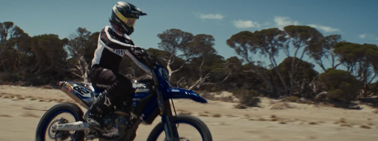 Close-up slow-motion tracking shot of a motocross rider racing across a sandy terrain