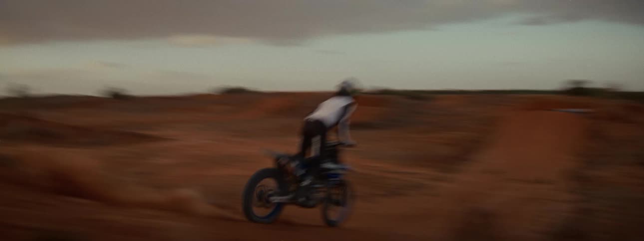 A motocross rider performs impressive jumps in slow motion on a dirt track as the sun sets