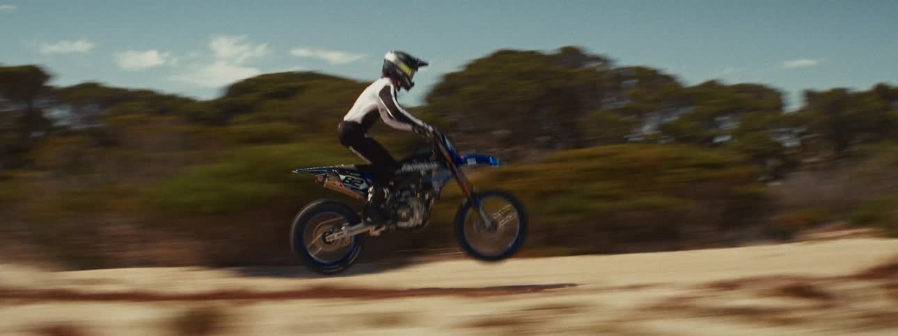 Slow-motion side view of a motocross rider speeding down a sandy track and performing a wheelie