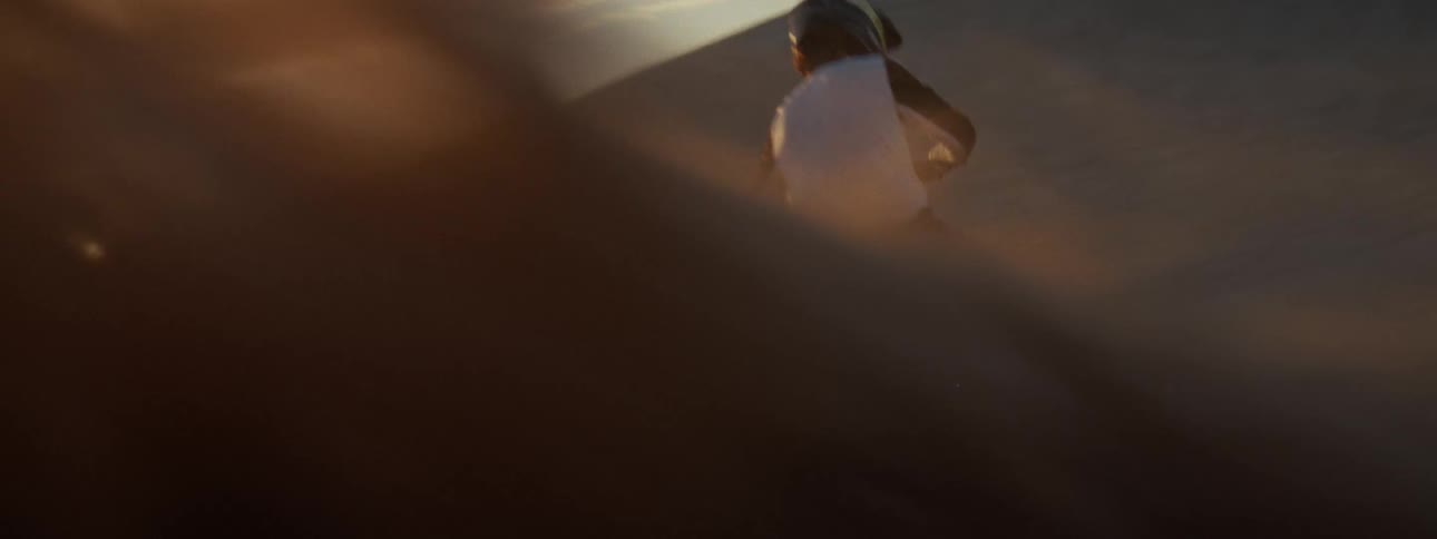 A motocross rider carves a turn on a massive sand dune, spraying sand into the air before riding off into the vast desert at sunset in slow motion