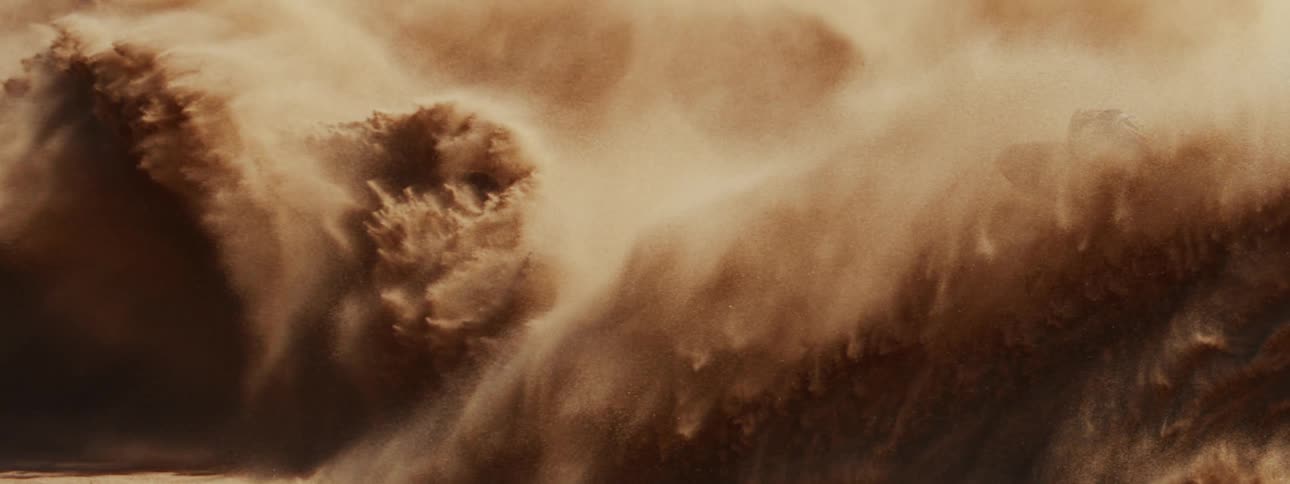 A powerful off-road vehicle sends a massive wave of sand flying through the air in a dramatic slow-motion close-up
