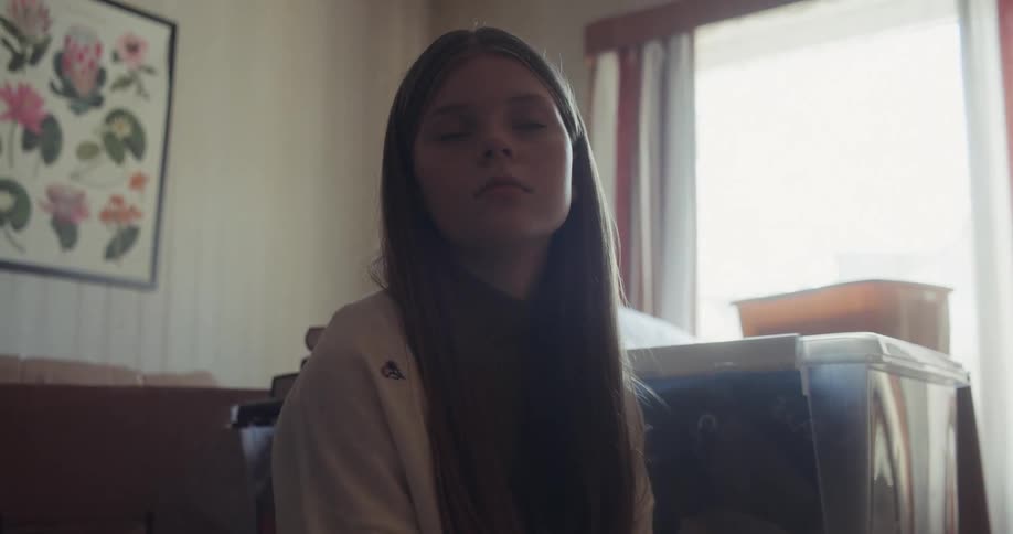 A solemn young girl looks thoughtfully around her room, which is filled with moving boxes