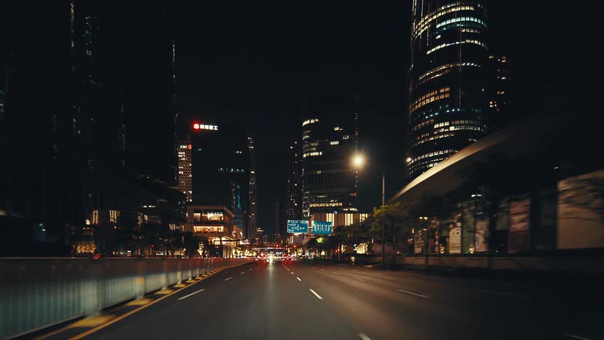 A point-of-view drive through a modern metropolis at night, gliding under an architectural overpass towards a glowing skyline of skyscrapers
