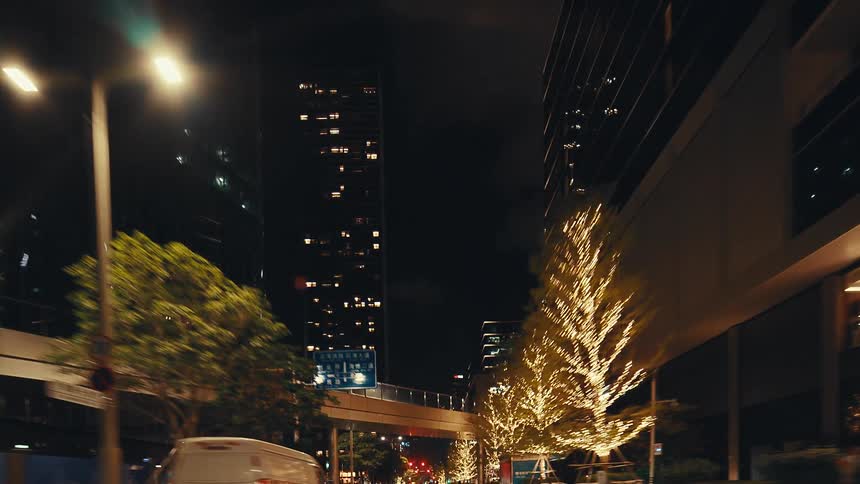 A slow-motion drive through a modern city at night, passing by skyscrapers and trees adorned with festive string lights